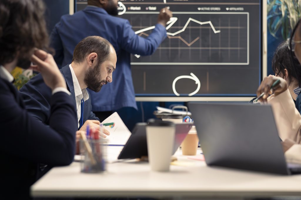 Corporate employees examining organizational progress during a meeting, conducting an analysis or benchmarking exercises. Business specialists discuss activities for expansion plans.